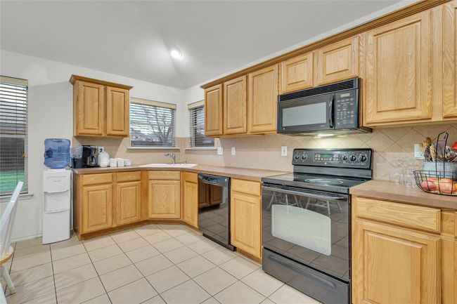 Kitchen with black appliances, vaulted ceiling, light countertops, and light brown cabinetry | Image 10