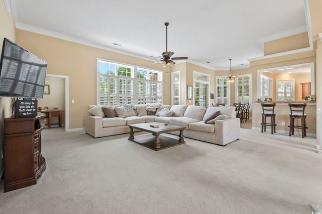 Living area with crown molding, a ceiling fan, carpet, and baseboards | Image 4