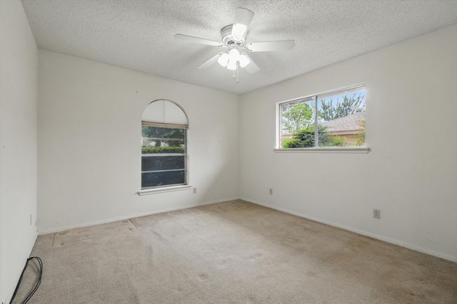 Carpeted empty room with a ceiling fan, a textured ceiling, and baseboards | Image 27
