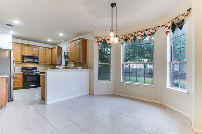 Kitchen with black appliances, backsplash, light countertops, light tile patterned floors, and decorative light fixtures | Image 9