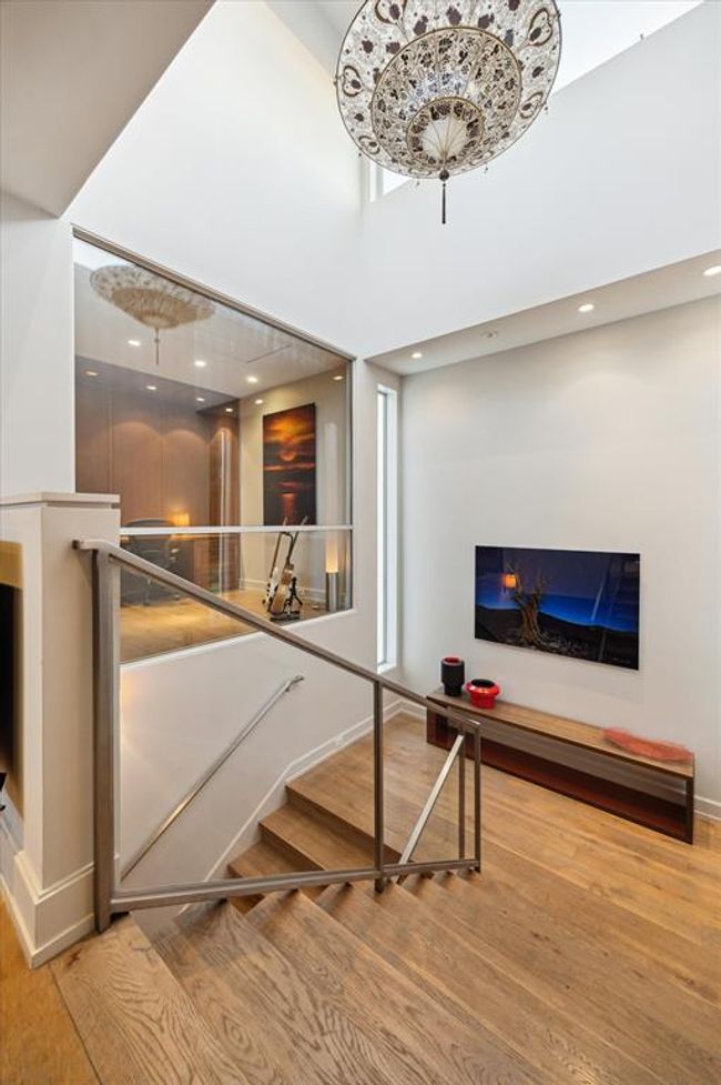 Let’s go up! The design of this home emphasizes natural light - and this staircase is a prime example—combining architectural elegance with functionality. The soaring ceilings, oversized window, and striking chandelier create a luminous transition space. To the left, a large interior window offers a glimpse into the office, enhancing the open, airy ambiance. | Image 25