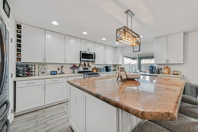 Kitchen featuring a kitchen bar, a center island, stainless steel appliances, white cabinets, and hanging light fixtures | Image 5