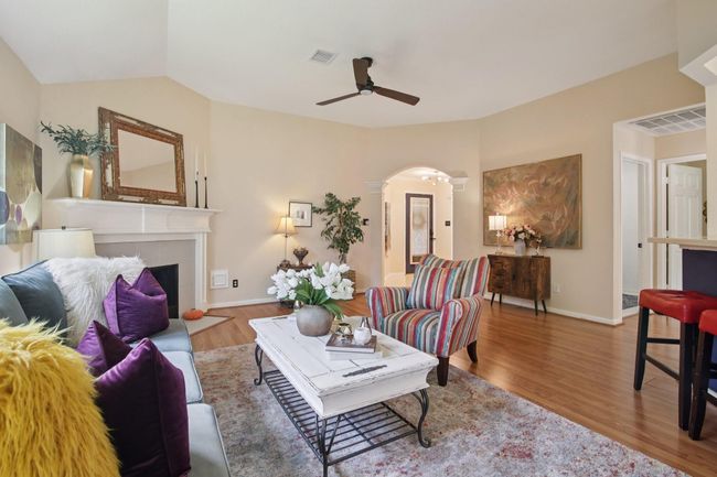 This inviting living room features warm-toned walls and wood flooring, with a cozy fireplace and ceiling fan. An open layout connects to adjoining areas. | Image 7