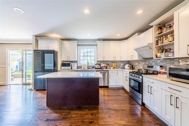 Kitchen with stainless steel appliances, exhaust hood, a sink, tasteful backsplash, and light countertops | Image 16