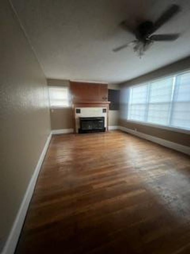 Unfurnished living room with wood finished floors, baseboards, a ceiling fan, and a fireplace | Image 5