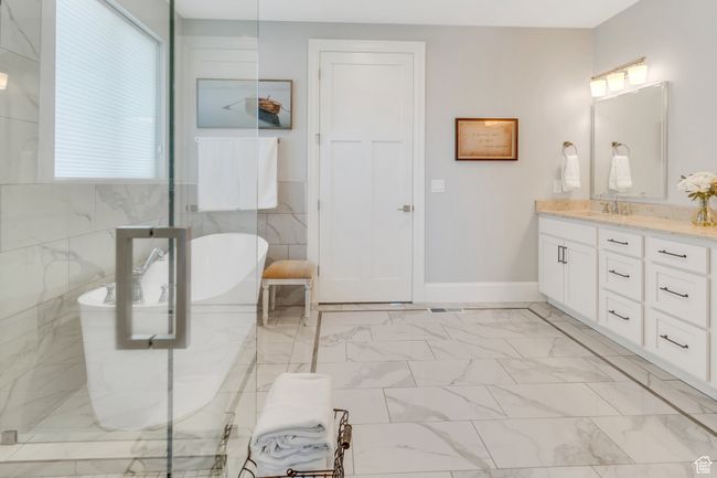 Bathroom featuring double vanity, a freestanding bath, marble look tile flooring, and a marble finish shower | Image 36