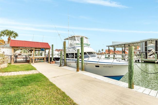 56 Marlin is a canal front property with a private dock, featuring a boat moored beside a well-maintained path. The setting includes a covered fishing station with a red roof and lush green lawn, ideal for boating enthusiasts. | Image 30