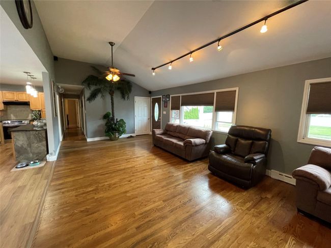 Living area featuring baseboard heating, track lighting, ceiling fan, light wood finished floors, and lofted ceiling | Image 10