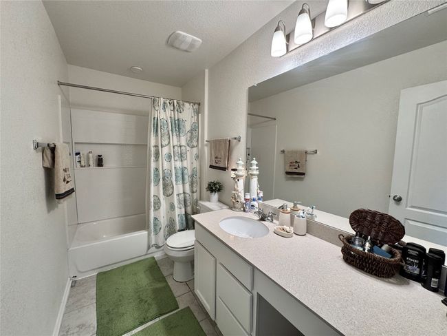 Full bathroom with vanity, shower / bath combo with shower curtain, tile patterned floors, and a textured wall | Image 29