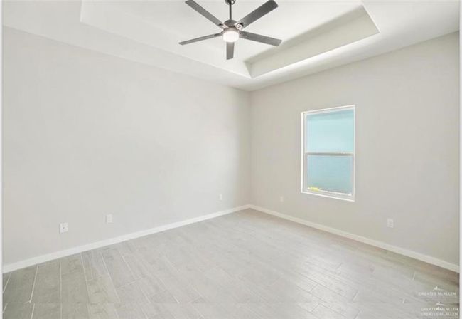 Empty room with light hardwood / wood-style floors, a tray ceiling, and ceiling fan | Image 10