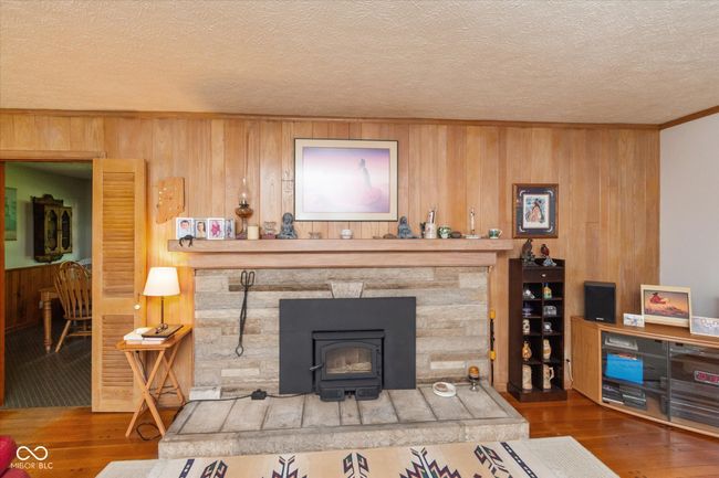 living room featuring wooden walls, wood finished floors, a textured ceiling, and crown molding | Image 8