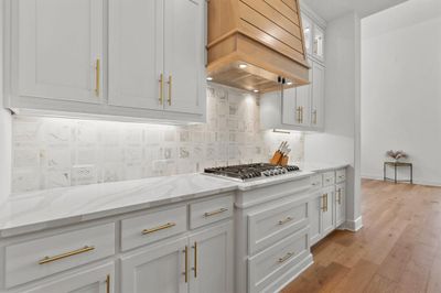 Kitchen featuring light stone countertops, light wood-type flooring, white cabinets, backsplash, and custom exhaust hood | Image 2