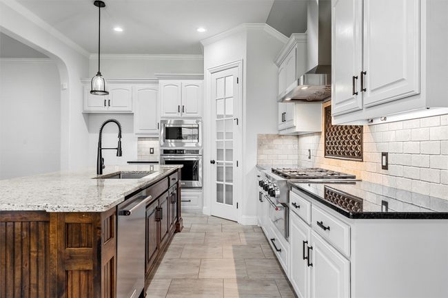 Kitchen with appliances with stainless steel finishes, wall chimney exhaust hood, dark stone countertops, crown molding, and decorative backsplash | Image 11