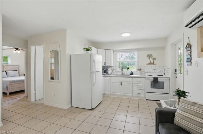 Kitchen featuring white appliances, light tile patterned floors, a wall mounted air conditioner, backsplash, and light countertops | Image 20