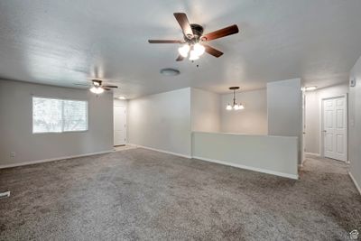 Spare room with ceiling fan with notable chandelier, light carpet, and a textured ceiling | Image 3