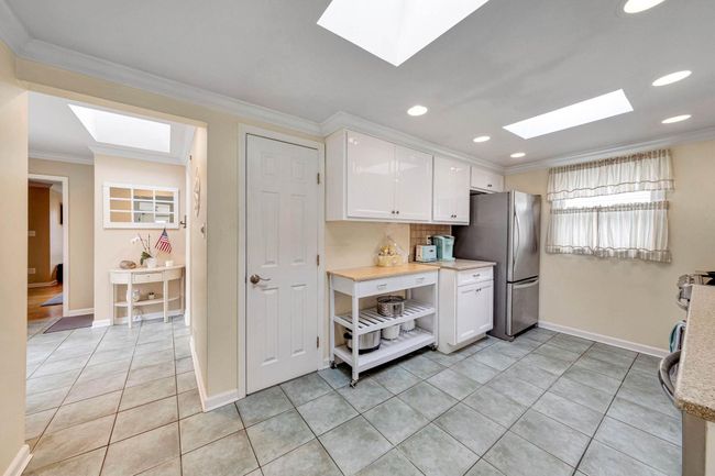 Kitchen featuring light countertops, ornamental molding, freestanding refrigerator, a skylight, and white cabinetry | Image 19