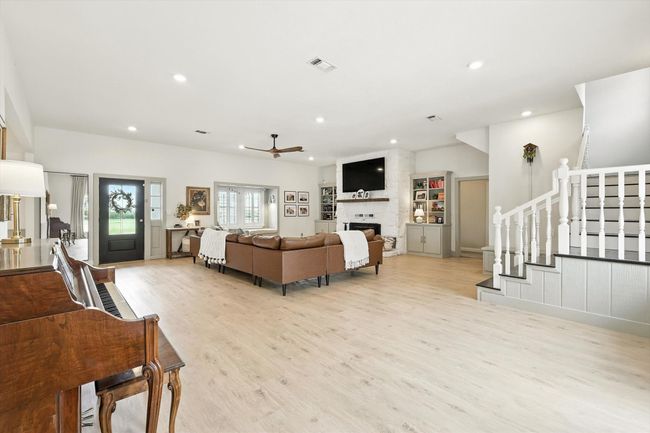 Living room with stairs, light wood-type flooring, a large fireplace, ceiling fan, and recessed lighting | Image 17