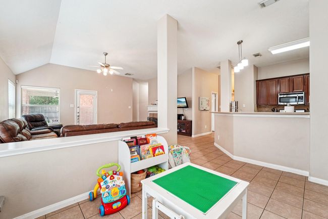 This open-concept living area features a cozy setup with a leather sectional, ceiling fan, and natural light from large windows. The kitchen offers stainless steel appliances and dark wood cabinets, with a breakfast bar for casual dining. A dedicated play area adds family-friendly functionality. | Image 13