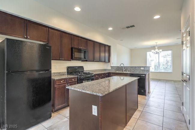 Kitchen featuring light stone counters, a center island, light tile patterned floors, a sink, and black appliances | Image 17