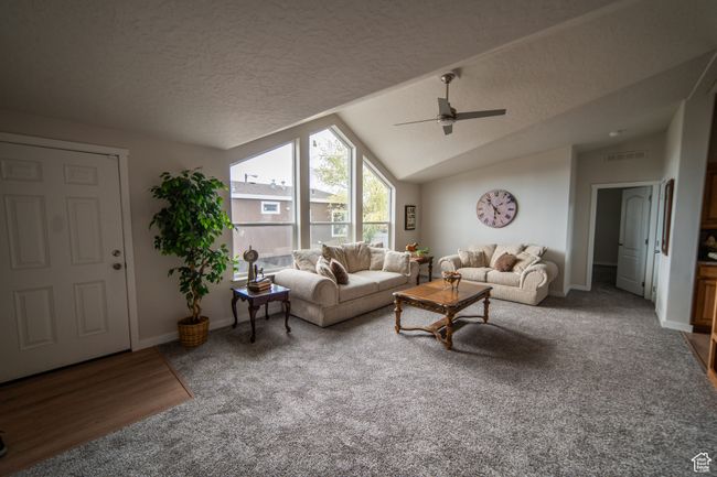 Carpeted living area featuring vaulted ceiling, a textured ceiling, ceiling fan, baseboards, and visible vents | Image 24