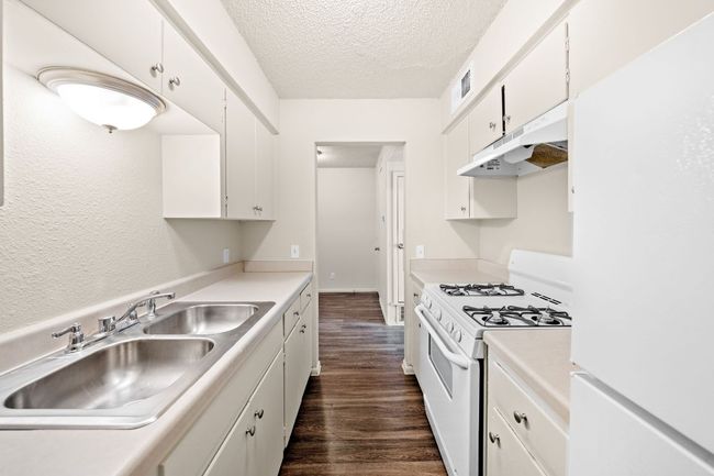 Kitchen featuring white appliances, dark wood-style flooring, under cabinet range hood, a textured ceiling, and a sink | Image 6