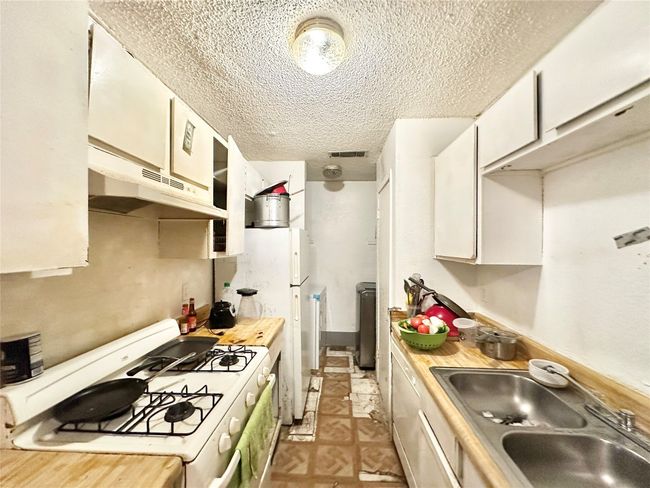 Kitchen featuring white gas stove, a sink, a textured ceiling, under cabinet range hood, and light countertops | Image 35