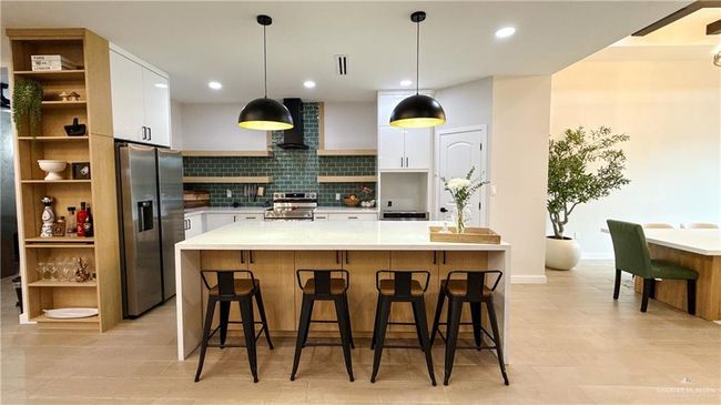 Kitchen featuring stainless steel appliances, wall chimney exhaust hood, white cabinets, decorative backsplash, and light countertops | Image 5