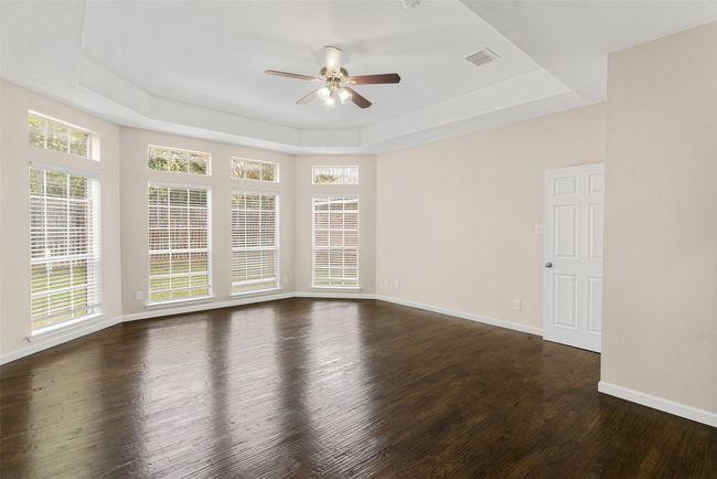 Empty room featuring a ceiling fan, a raised ceiling, baseboards, visible vents, and dark wood-style flooring | Image 22