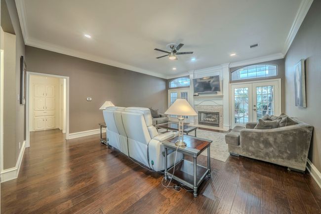 Living room featuring a ceiling fan, ornamental molding, dark wood-style flooring, a fireplace, and plenty of natural light | Image 5