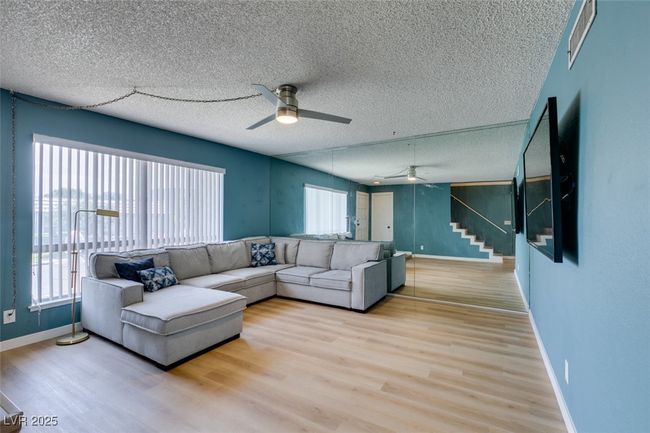 Living area featuring ceiling fan, stairway, plenty of natural light, wood finished floors, and a textured ceiling | Image 6
