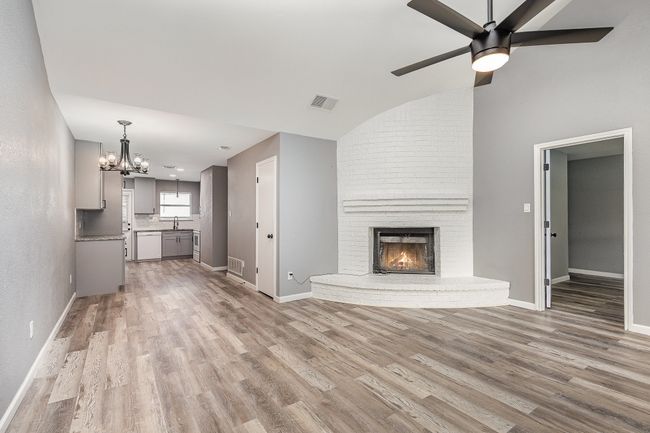 Unfurnished living room with wood finished floors, a chandelier, a brick fireplace, ceiling fan, and baseboards | Image 11