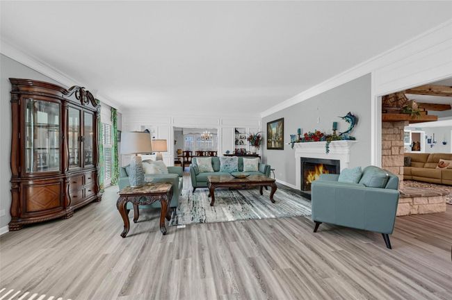Living area with wood finished floors, ornamental molding, a lit fireplace, a chandelier, and baseboards | Image 8