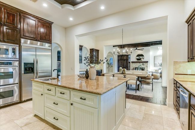 Kitchen featuring a large size island with custom cabinetry, granite counter tops, bar sink, custom range hood, double ovens, a sink, a tray ceiling, and built in appliances | Image 15