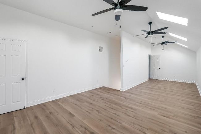 Additional living space featuring baseboards, a ceiling fan, wood finished floors, and vaulted ceiling with skylight | Image 20