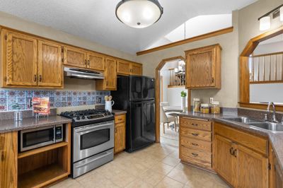 A chef’s dream, the kitchen boasts stainless steel appliances, ample oak cabinetry blending functionality with design. The tile flooring completes the space, offering durability and style. | Image 2