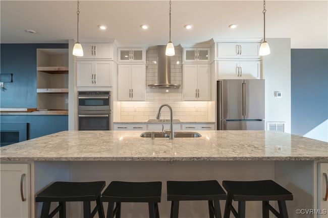 Kitchen featuring hanging light fixtures, appliances with stainless steel finishes, a center island with sink, and wall chimney exhaust hood | Image 7