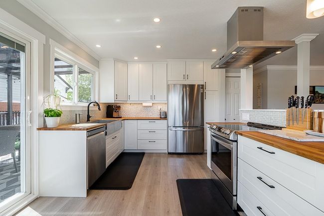 Kitchen with stainless steel appliances, butcher block countertops, island range hood, light wood-style flooring, and white cabinets | Image 12