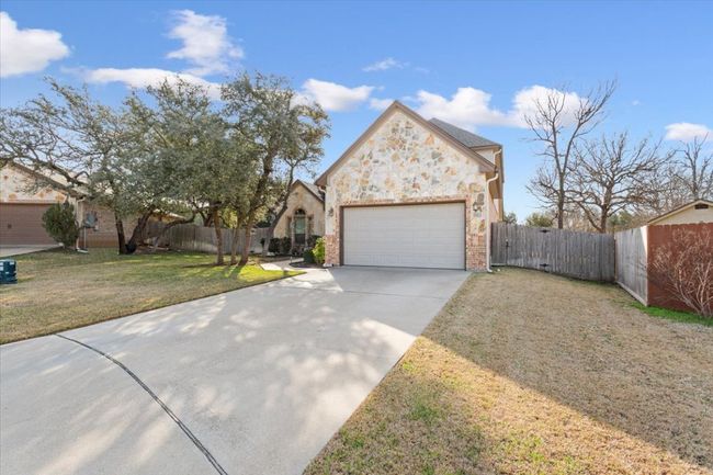View of front of home with a front lawn, stone siding, fence, concrete driveway, and an attached garage | Image 4