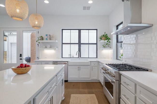 Kitchen with open shelves, stainless steel appliances, ventilation hood, wood finished floors, and decorative backsplash | Image 10