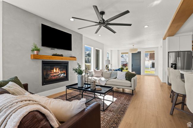 Living area with light wood-style floors, a glass covered fireplace, a ceiling fan, recessed lighting, and a textured ceiling | Image 15