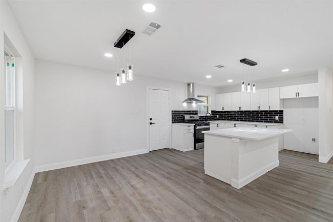 Kitchen with white cabinets, hanging light fixtures, stainless steel stove, a center island, and light hardwood / wood-style floors | Image 7
