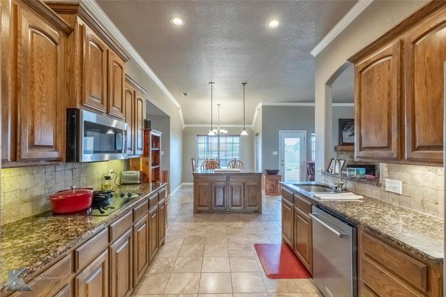 Kitchen featuring stainless steel appliances, a sink, ornamental molding, tasteful backsplash, and brown cabinetry | Image 11