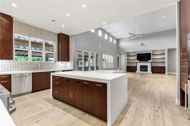 Kitchen featuring stainless steel dishwasher, ceiling fan, a high ceiling, a fireplace, and light countertops | Image 8