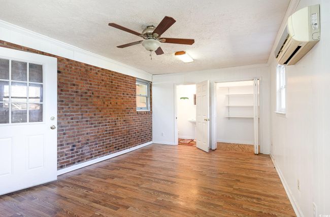 Unfurnished bedroom with brick wall, multiple windows, wood-type flooring, a wall unit AC, and a textured ceiling | Image 9