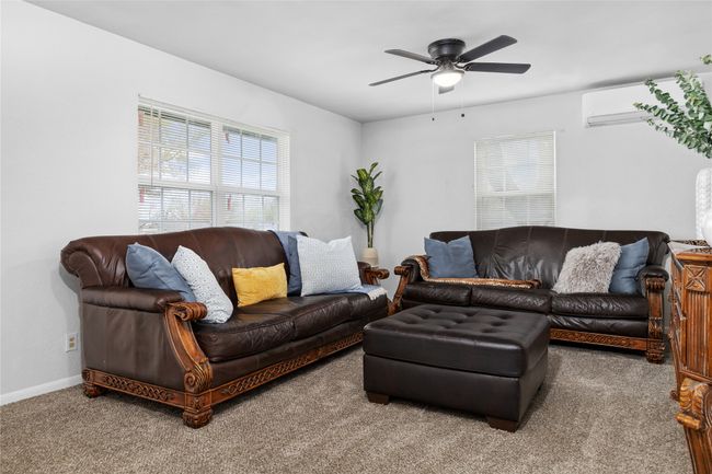Carpeted living room featuring a ceiling fan, a wall unit AC, and baseboards | Image 17
