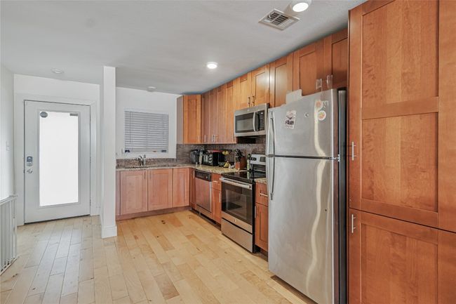 Kitchen with stainless steel appliances, light stone counters, light wood-type flooring, and backsplash | Image 6