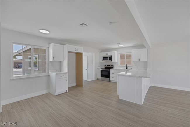 Kitchen with appliances with stainless steel finishes, a peninsula, white cabinets, light wood-style floors, and healthy amount of natural light | Image 7