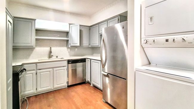 Kitchen featuring sink, light wood-type flooring, appliances with stainless steel finishes, stacked washing maching and dryer, and backsplash | Image 14
