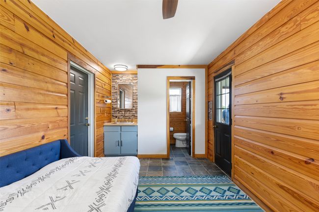 Bedroom with wood walls, dark stone finish floors, connected bathroom, and a ceiling fan | Image 32