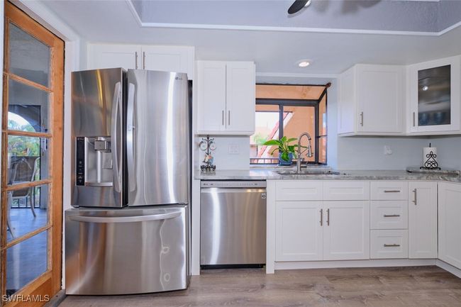 Kitchen with stainless steel appliances, white cabinetry, light wood-type flooring, glass insert cabinets, and recessed lighting | Image 17